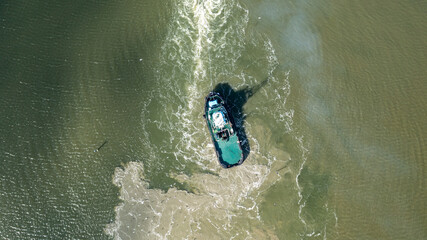 Aerial top down view of tug boat manoeuvring in murky shallow  water. Bottom sediment surfacing due to propeller wash.