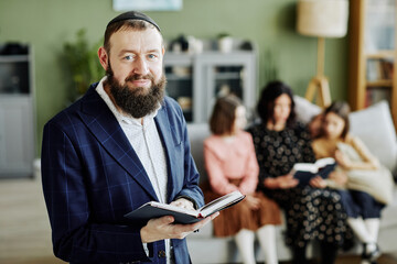 Waist up portrait of bearded jewish man wearing kippah and looking at camera holding book, copy...