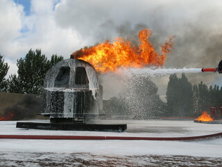 Helicopter fire fighting training. Non aspirated foam branch spraying heavy foam blanket on flaming...