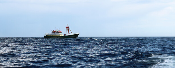 Side view of green hulled standby safety vessel making way ahead in overcast weather. Vessel is used to assist and guard oil and gas seismic survey exploration operations.