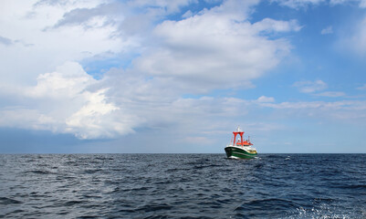 Front view of green hulled standby safety vessel making way ahead with storm clouds in the background. Vessel is used to assist oil and gas seismic survey exploration operations.