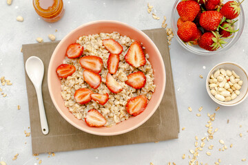 Oatmeal porridge with summer strawberries berries. Porridge oats in bowl with honey,milk,nuts. Healthy food breakfast,lifestyle,dieting, proper nutrition. Top view flat lay on gray table background