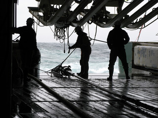 Silhouettes of persons recovering source (gun) array on seismic survey vessel. Sources are used to produce underwater acoustic sound waves with high pressure air.