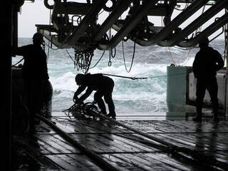 Silhouettes of persons recovering source (gun) array on seismic survey vessel. Sources are used to...