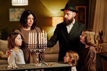 Portrait of orthodox jewish family lighting menorah candle during Hanukkah celebration at home