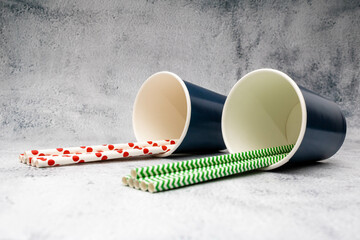 Red and green paper straws inside two blue cups. Mention the sustainable party, replacement of plastic in people's routine and get-togethers for actions in support of the environment.