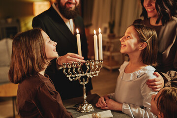 Portrait of orthodox jewish family lighting menorah candle together during Hanukkah celebration...