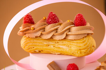Eclairs cakes with cream and raspberries on a brown background. custard cakes.