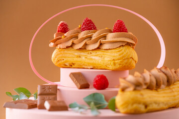Eclairs cakes with chocolate cream and raspberries on a brown background. custard cakes.