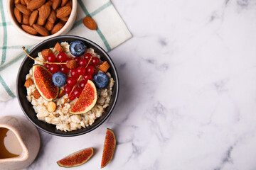 Bowl of oatmeal with berries, almonds and fig pieces on white marble table, flat lay. Space for text