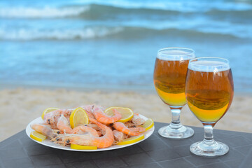 Cold beer in glasses and shrimps served with lemon on beach