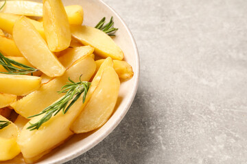 Plate with tasty baked potato wedges and rosemary on grey table, closeup. Space for text