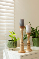 Pair of beautiful wooden candlesticks and houseplants on white table in room
