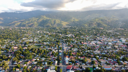 Fototapeta na wymiar Aerial view of capital city Dili, Timor Leste in Southeast Asia surrounded by rugged hilly landscape, colorful tin roofed houses and buildings with tree greenery spreading throughout the city