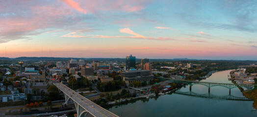 aerial shot of the Henley Street Bridge and Gay Street Bridge over the Tennessee River surrounded by autumn colored trees, lush green trees and office buildings with powerful clouds at sunset - obrazy, fototapety, plakaty