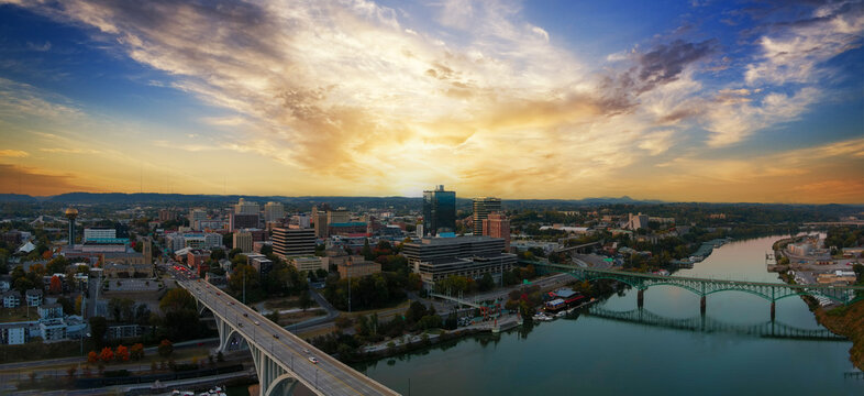 aerial shot of the Henley Street Bridge and Gay Street Bridge over the Tennessee River surrounded by autumn colored trees, lush green trees and office buildings with powerful clouds at sunset