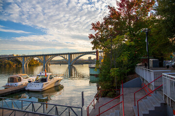 a gorgeous autumn landscape along the Tennessee River with boats docked and the Henley Street Bridge over the water with blue sky and clouds at sunset in Knoxville Tennessee USA - obrazy, fototapety, plakaty