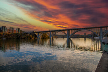 Fototapeta na wymiar the Henley Street Bridge over the Tennessee River surrounded by autumn colored trees, lush green trees and office buildings with powerful clouds at sunset in Knoxville Tennessee USA