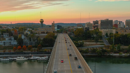 an aerial shot of cars driving on the Henley Street Bridge surrounded by the Sunsphere, skyscrapers, office buildings, autumn colored trees and lush green trees at sunset in Knoxville Tennessee USA - obrazy, fototapety, plakaty