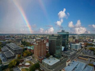 an aerial shot of the glass skyscrapers and office buildings in the city skyline surrounded by autumn colored trees and lush green trees with blue sky, clouds and a rainbow in Knoxville Tennessee USA - obrazy, fototapety, plakaty
