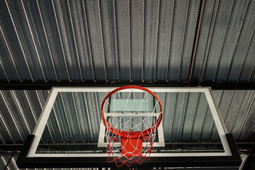 View from bottom of Basketball fiber backboard, Hoop red metal ring and white net against Ceiling sheet metal in the gym. Empty basketball basket, Space for text, Selective focus.