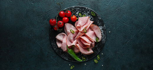 Board with slices of delicious ham and vegetables on dark background, top view