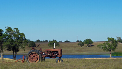Old rusted farmall-type tractor with mowing deck attached sitting in field by a stock tank - closeup with abundant blue sky space for text