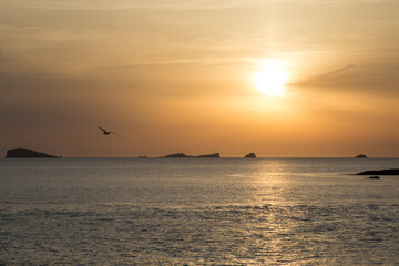 Naklejka na ściany i meble Sunset on the island of Ibiza with the sun setting on the horizon and orange colors in the sky