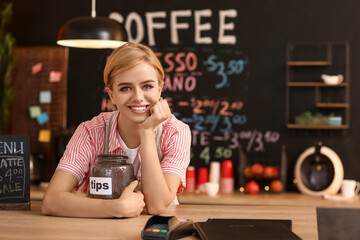 Young female barista with tip jar at table in cafe