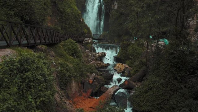 Slow Tilt Up View Of Cascading Peguche Waterfall With Wooden Walkway Bridge In Otavalo, Ecuador 
