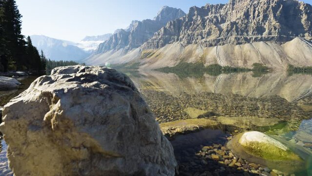 Crystal clear lake with mountains on sunny day. Handheld slow motion movement, wide low angle. Lakeside, Bow Lake, Icefields Parkway, Canadian Rockies, Canada.