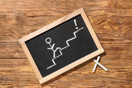 Chalkboard with drawing of person and ladder on wooden background