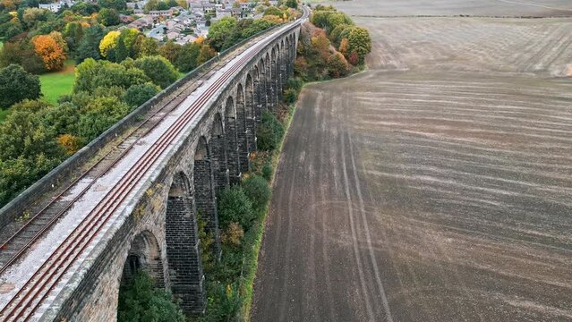 Sweeping drone footage of the Penistone Railway Station and Viaduct near Barnsley, South Yorkshire. Showing a ploughed field, bridge, woodland and railway tracks.