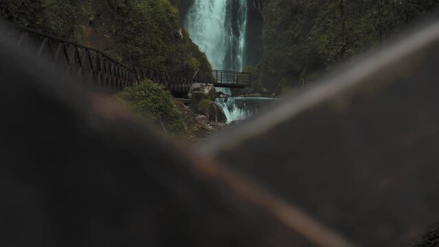 View Of Cascading Peguche Waterfalls In Otavalo. Ascending Shot Behind Bridge Fence