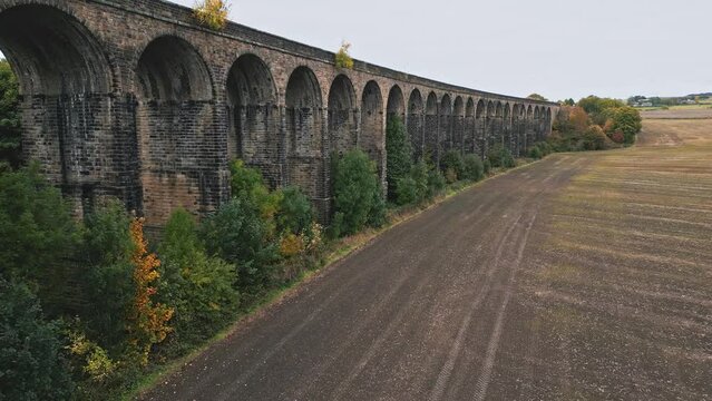 Low drone footage of the Penistone Railway Station and Viaduct near Barnsley, South Yorkshire. Showing a ploughed field, bridge, woodland and railway tracks.