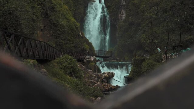 View Of Cascading Peguche Waterfalls In Otavalo. Pedestal Down Behind Bridge Fence