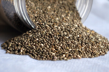 Close-up of chia seeds scattered from glass jars on white background. Copy space.