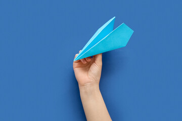 Woman with blue paper plane on color background