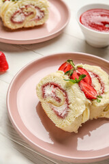 Plate with slices of tasty strawberry roll cake on light wooden table, closeup