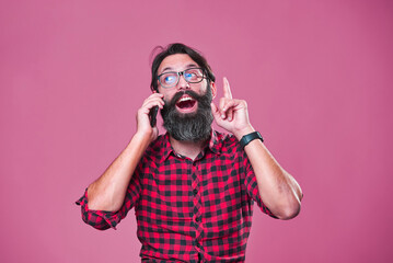 Bearded man with glasses coming up with solution, idea realization while talking on the phone; pink...