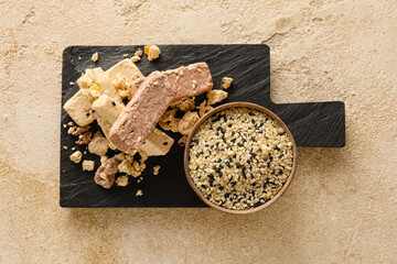 Board with bowl of sesame seeds and halva on light background