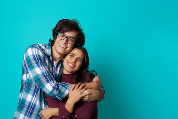 Fototapeta premium Happy couple in love hugging, embracing each other; casual wear, teenage years, fresh relationship; teal studio background