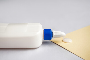 Bottle of glue and paper sheet on grey background, closeup