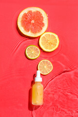 Bottle of vitamin C serum and fruits in water on red background