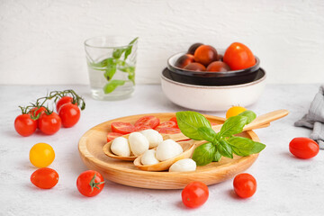 Wooden plate with tasty mozzarella cheese and fresh tomatoes on light table