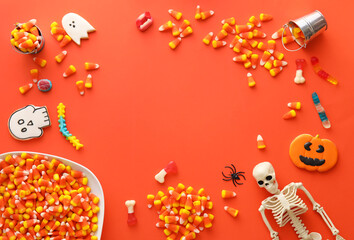 Frame made of Halloween candies, cookies and skeleton on red background