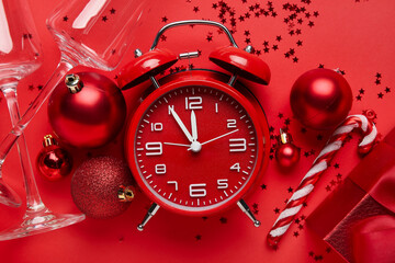 Vintage alarm clock with Christmas decor and glasses on red background