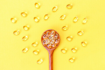 Vitamin D3 capsules on wooden spoon on a yellow background close-up.