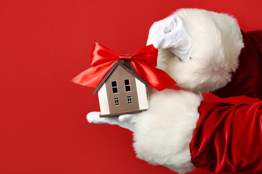 Santa Claus with house model and bow on red background