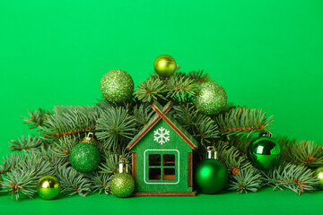 House figure with Christmas balls and fir branches on green background